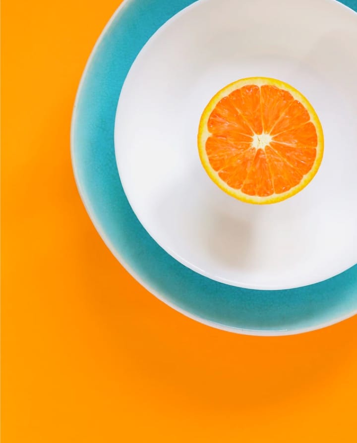 Image of orange slice on a white plate on a orange colored table