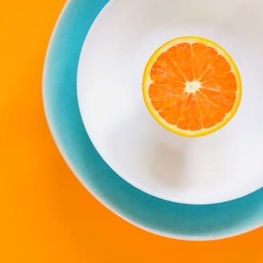 Image of orange slice on a white plate on a orange colored table